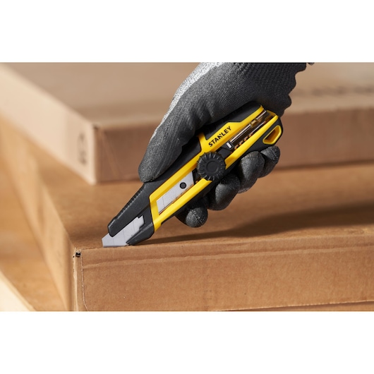 Photo of STANLEY STHT10500-0 utility knife with yellow and black handle cutting cardboard, held by gloved hand.