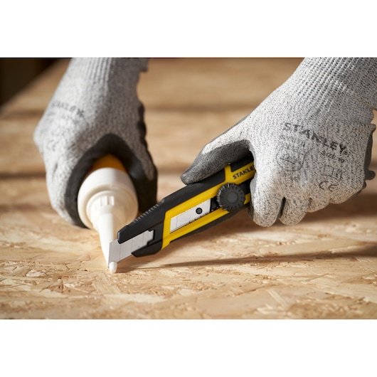 Photo of STANLEY STHT10500-0 utility knife being used on plywood, hands wearing gray gloves.