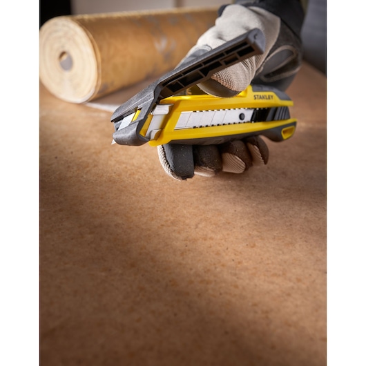STANLEY STHT10501-0 utility knife in yellow and black held by gloved hand on work surface, side angle.
