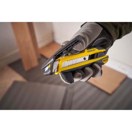Photo of STANLEY STHT10501-0 utility knife, yellow and black, held in gloved hand, product close-up.