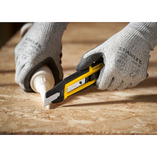 Photo of STANLEY STHT10501-0 utility knife cutting on a wooden surface, held by gloved hands.