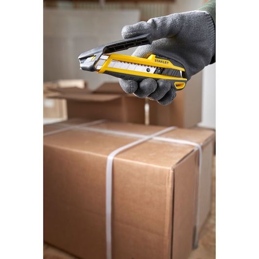 Photo of STANLEY STHT10501-0 utility knife held above cardboard boxes in a warehouse setting.