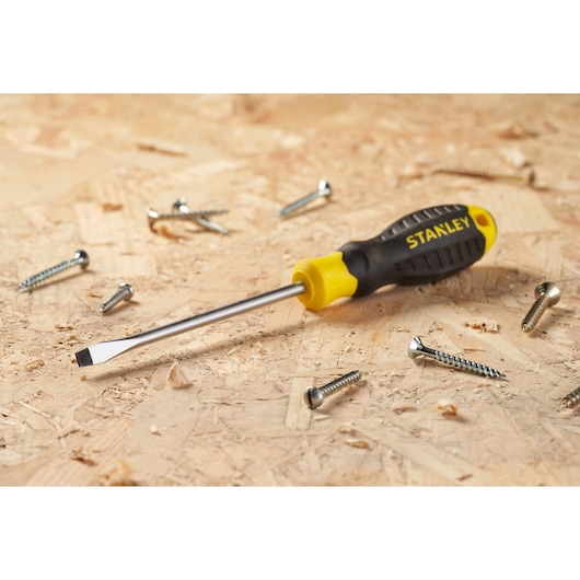 STANLEY STHT16146-0 flat-head screwdriver with black and yellow handle on wood surface with screws.