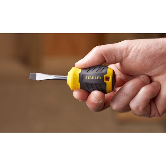 Photo of STANLEY STHT16147-0 stubby flathead screwdriver with yellow and black handle held in hand.