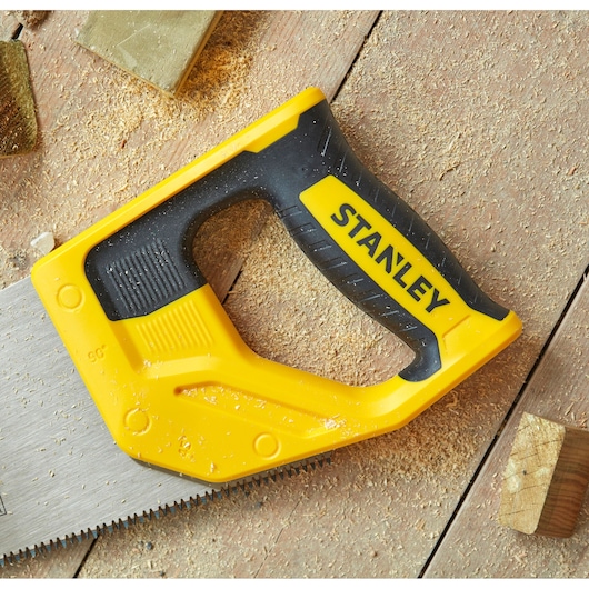 Photo of STANLEY STHT20348-1 hand saw with yellow and black handle on wood surface with sawdust.