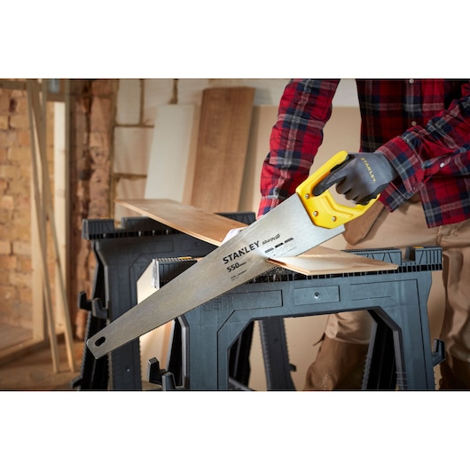 STANLEY STHT20372-1 hand saw with yellow handle cutting wood in workshop setting.