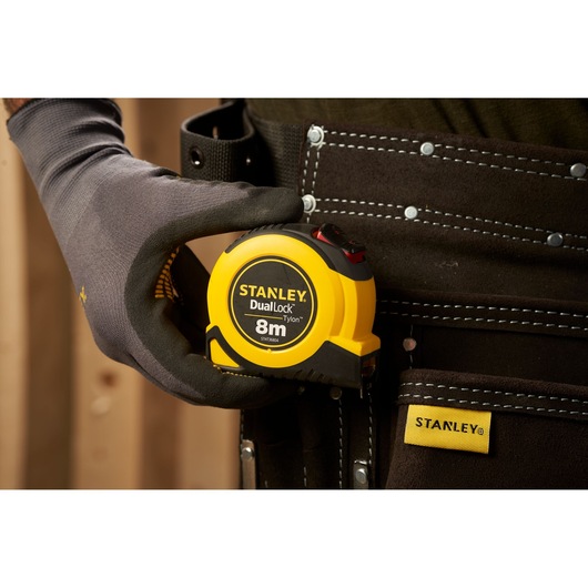 Photo of STANLEY STHT36804-0 DualLock 8m tape measure in tool belt, held by gloved hand.