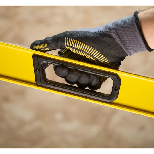 A close-up of a gloved hand holding a yellow spirit level by its handle.