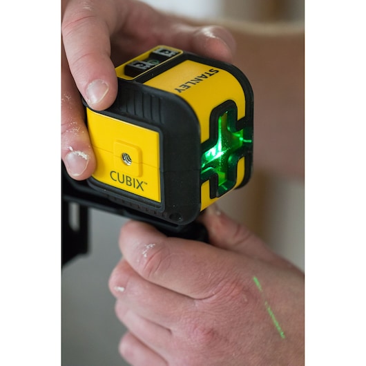 Stanley STHT77499-1 Cubix laser level in use, yellow and black casing, emitting green cross lines.