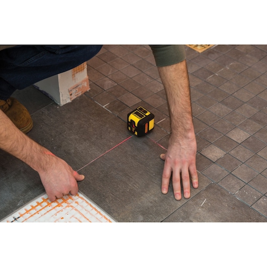 STANLEY STHT77502-1 laser level used for tile alignment on a brown floor, close-up view.