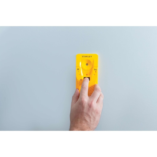 Stanley STHT77587 stud finder tool in use against a light wall, close-up photography showing hand operation.