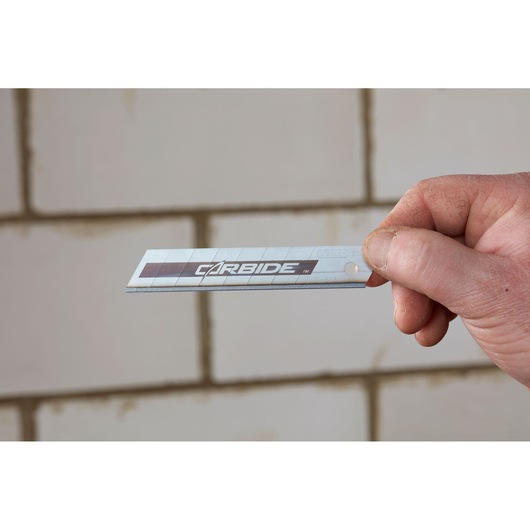 Photo of STANLEY STHT8-11818 carbide utility blade held in hand with tiled wall background.