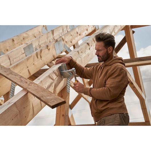 Photo of a person using a STANLEY hammer on wooden beams during construction.