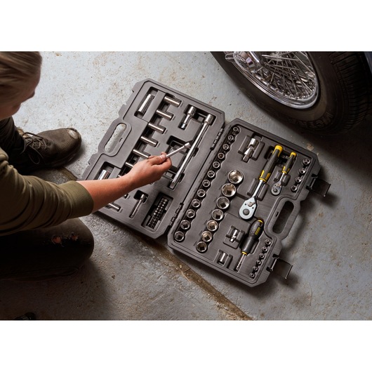 STANLEY STMT82831-1 ratchet and socket set with 72 pieces in black case, open on garage floor next to a car.