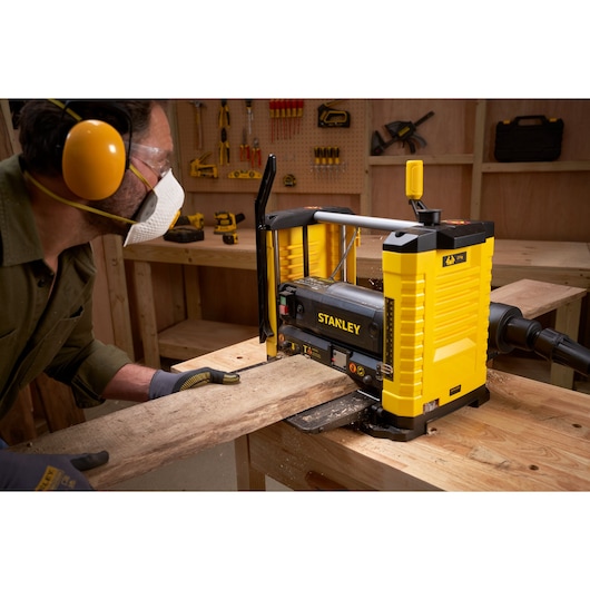 Photo of STANLEY STP18-B2 planer used to flatten a wooden board in a workshop, with safety gear visible.