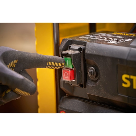 STANLEY STP18-B2 machine power switch with gloved hand pressing green button, close-up angle.
