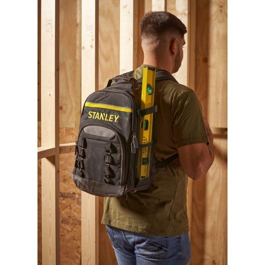 Stanley STST1-72335 black and yellow backpack worn by a man in a workshop, holding a level tool.