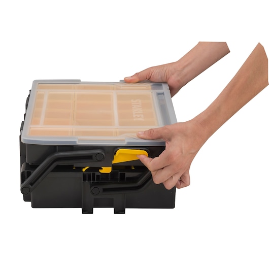 STANLEY STST1-75540 organizer box with transparent lid, black and yellow, hands opening front latch, front angle.