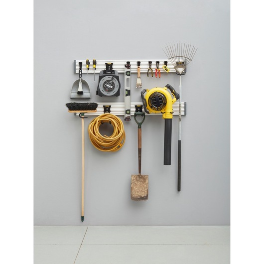 STANLEY STST22000-1 wall-mounted organizer rail holding various tools including rake, blower, broom, cord, and hand tools.