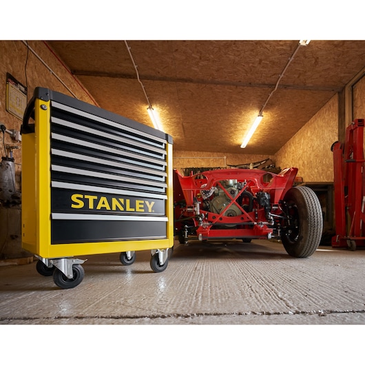 STANLEY STST74306-1 yellow and black rolling tool chest in garage, low angle, near red car frame.
