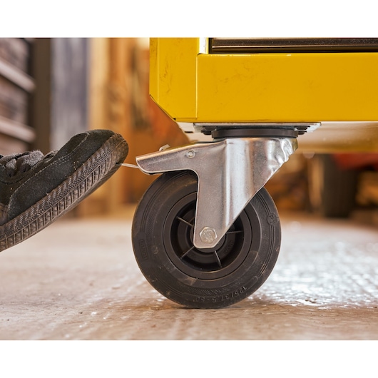 STANLEY STST74306-1 photography of yellow tool chest caster wheel with foot pressing brake lever, side angle.