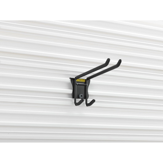 STANLEY STST82606-1 black steel wall hook with two prongs, mounted on white ribbed wall, front angle.