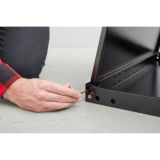 STANLEY STST97595-1 person assembling black metal frame with hex key, close-up on hand and corner joint.