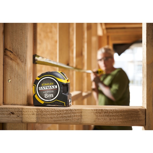 Photo of STANLEY FATMAX XTHT0-33501 8m tape measure on wooden frame at construction site.