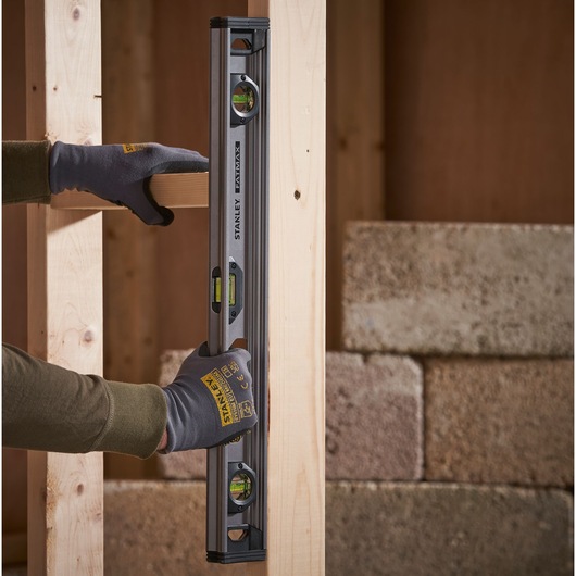 Photo of STANLEY XTHT1-42131 spirit level held vertically on wooden frame, with gloved hands.